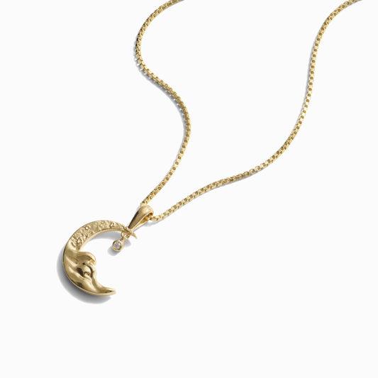 Gold necklace with crescent moon pendant and small diamond accent on a white background.