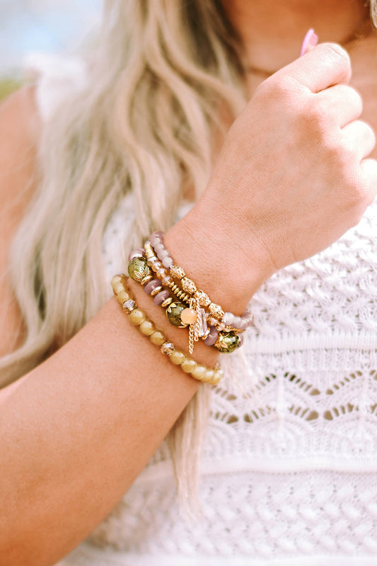 Set of multicolored beaded bracelets with gold accents worn on a woman's wrist, with a white crocheted top in the background.