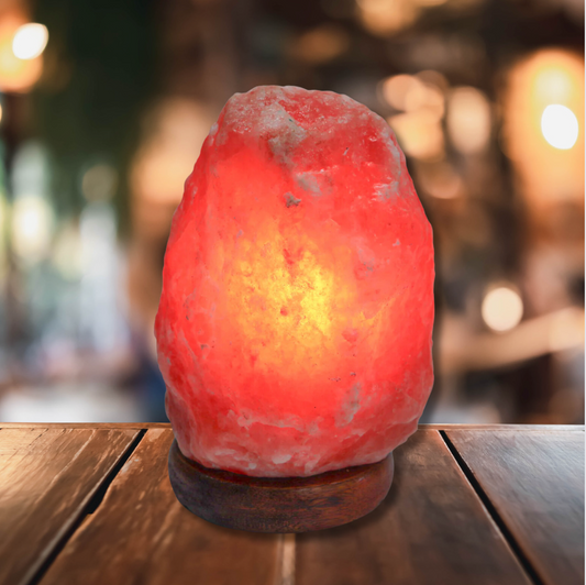 Red Himalayan salt lamp with a warm glow, placed on a wooden table with a blurred background.
