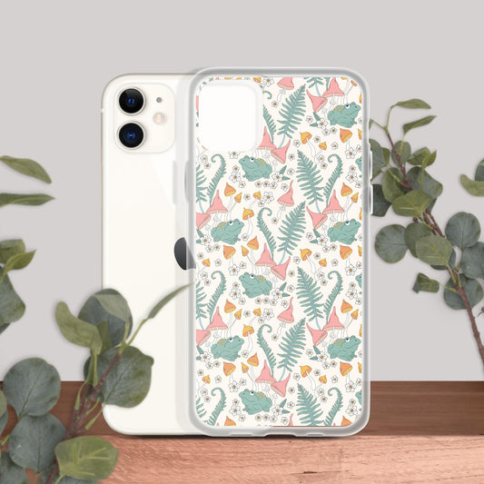 Clear case for iPhone 11 with whimsical botanical and frog design, shown on a white iPhone against a wooden surface and plant backdrop.