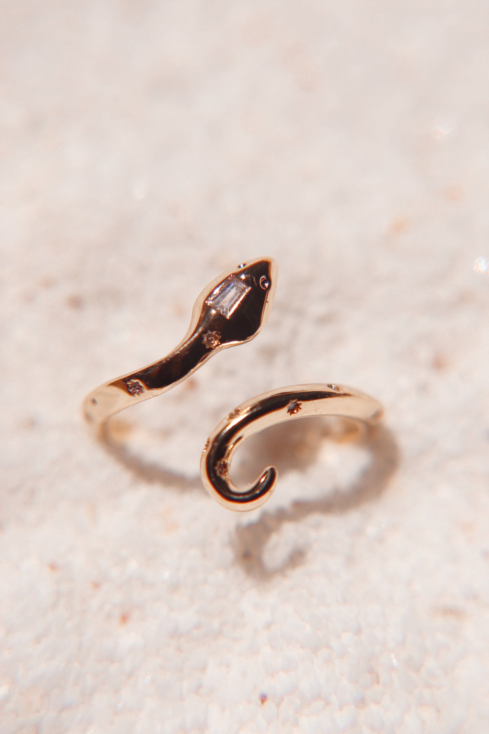 Gold snake ring with embedded gemstones displayed on a textured light-colored surface.