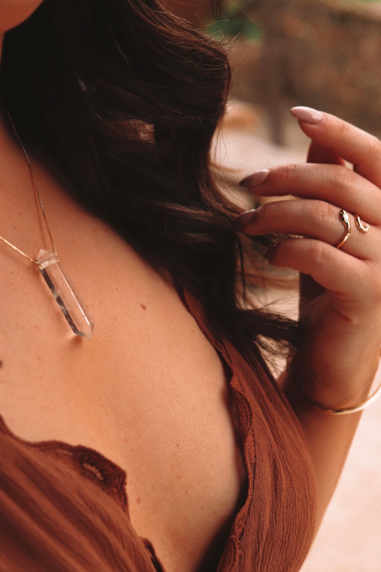 Crystal pendant necklace worn on a woman in a brown dress, showcasing a gold snake ring on her finger.
